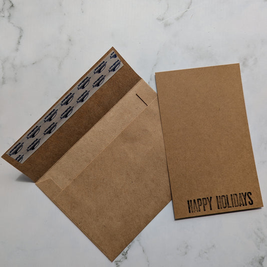 Brown envelope with self seal strip and 'Happy Holidays' card on a marble surface