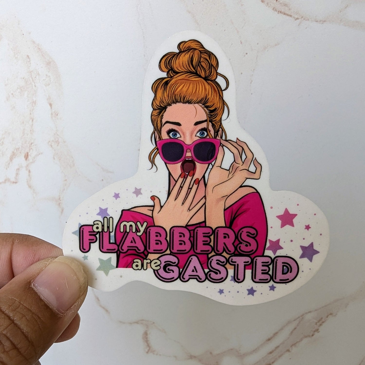 Sticker with a cartoon character and text held by a hand on a marble surface