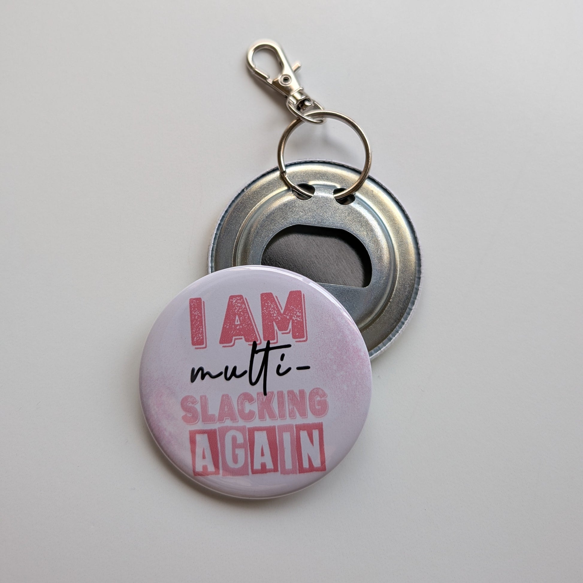 Keychain with bottle opener and 'I am multi-slacking again' text on a light gray background
