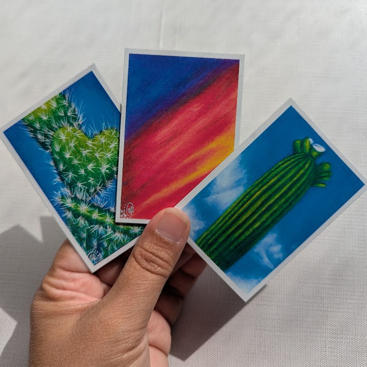 Hand holding three small cards with cactus illustrations on a white background